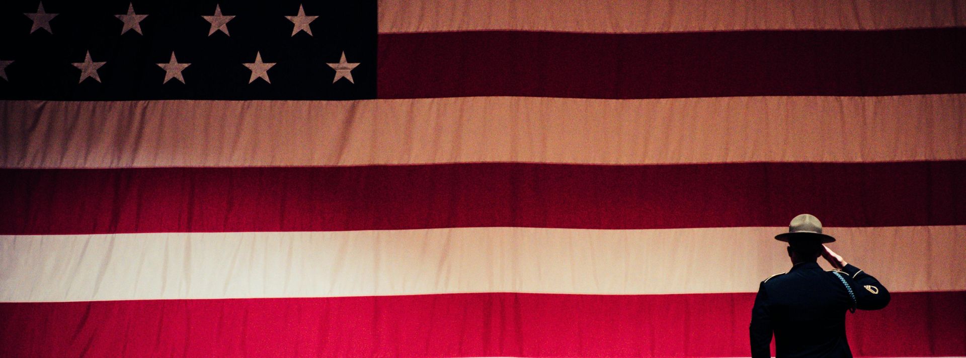 A solemn moment as a soldier salutes the American flag during a ceremony inside an auditorium.