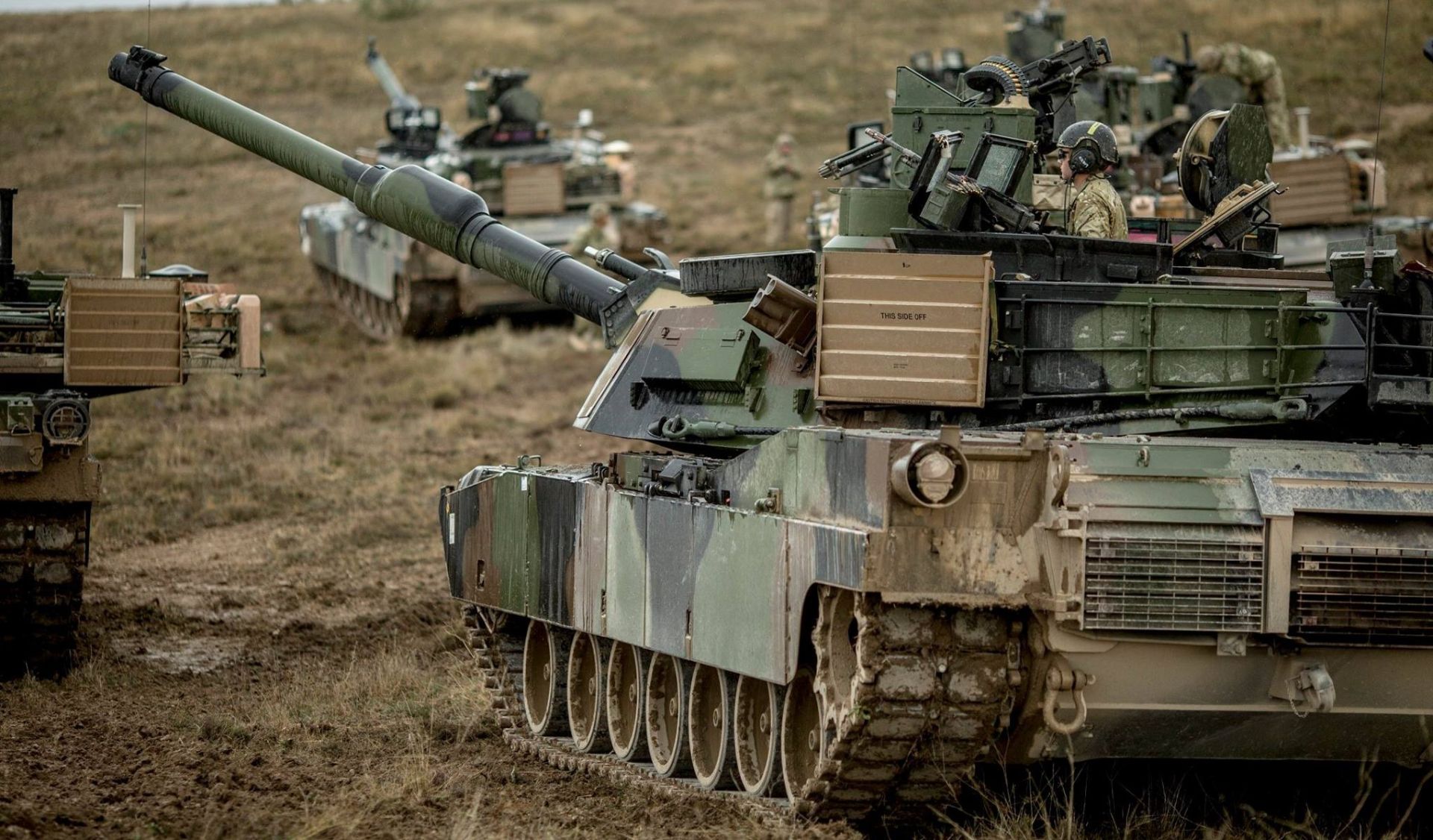 Three soldiers in camouflage gear with rifles in an outdoor military training exercise.